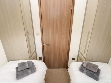 A bedroom with two single beds towels on beds wardrobes on each side and a wooden door at Hafan Lodge 85 Wisemans Bridge near Saundersfoot