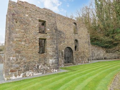 A stone ruin building with arched doorways and windows next to a lawn and trees at Hafan Lodge 85 Wisemans Bridge near Saundersfoot