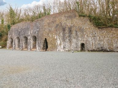 A stone wall with arched openings and a gravel ground in front surrounded by trees at Hafan Lodge 85 Wisemans Bridge near Saundersfoot