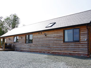 An exterior view of a wooden building with multiple windows and a gravel ground at Haimwood Byetake in Llandrinio