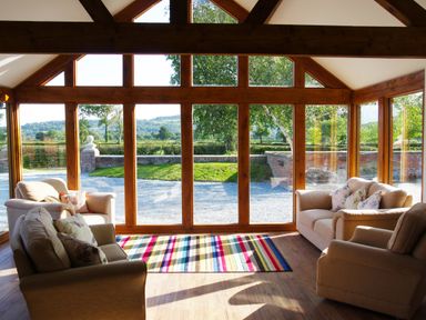 A room with large wooden framed windows beige sofas and a colorful striped rug at Haimwood Byetake in Llandrinio