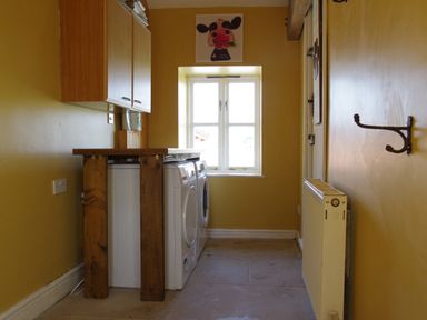 A laundry room with a washer and dryer under a wooden countertop and a window with a cow painting above at Haimwood Byetake in Llandrinio