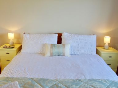 A bedroom with a bed with white bedding and two pillows a small blue decorative cushion and bedside tables with lamps at Haimwood Byetake in Llandrinio