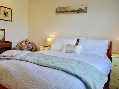 A bedroom with a double bed two bedside tables lamps a chair with a patterned cushion and wall art at Haimwood Byetake in Llandrinio
