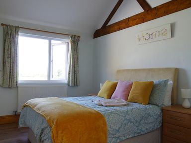 A bedroom with a bed with yellow and pink pillows and a yellow throw near a window with floral curtains at Haimwood Byetake in Llandrinio