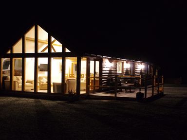 A house with large windows showing a lit living room and dining area and an outdoor seating area at Haimwood Byetake in Llandrinio