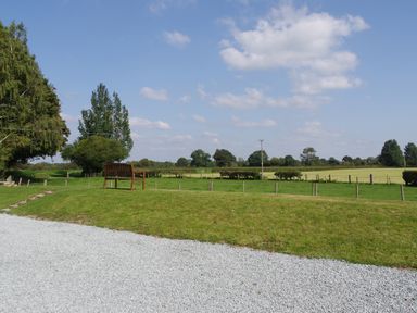 A wooden bench on a grassy area next to a gravel path with fields and trees in the background at Haimwood Byetake in Llandrinio