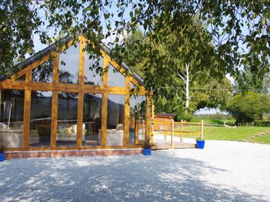A wooden house with large glass windows showing sofas inside and gravel in front at Haimwood Byetake in Llandrinio