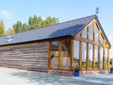 A wooden building with large glass windows and a slate roof surrounded by trees and gravel at Haimwood Byetake in Llandrinio