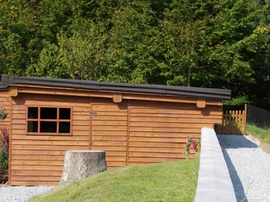 A wooden shed with a window and door surrounded by grass trees and a gravel path at Haimwood Byetake in Llandrinio