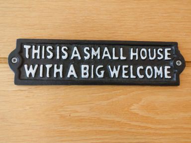 A black sign with white text saying this is a small house with a big welcome on a wooden surface at Hardings cottage in Minehead