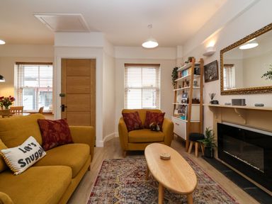 A living room with yellow sofas a wooden coffee table a fireplace a mirror and a bookshelf at Hardings cottage in Minehead