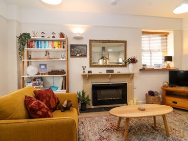 A living room with a yellow sofa red cushions a wooden coffee table fireplace bookshelf and a television at Hardings cottage in Minehead