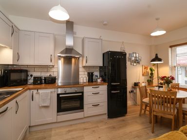 A kitchen with white cabinets wooden countertops a black smeg fridge a dining table with wooden chairs and flowers at Hardings cottage in Minehead