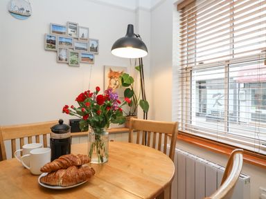 A dining area with a wooden table and chairs with croissants flowers and coffee maker at Hardings cottage in Minehead