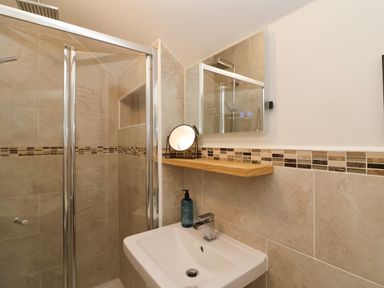 A bathroom with a glass shower enclosure a sink with a faucet a mirror and a wooden shelf with a small round mirror and a soap dispenser at Hardings cottage in Minehead