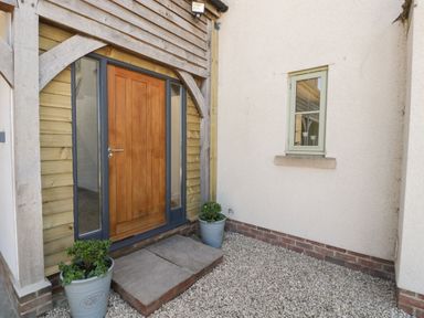 An exterior wooden door with glass side panels between two potted plants and a small window on a white wall at Little Knaplock in Fiddington near Combwich Somerset
