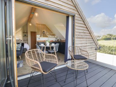 A balcony with two chairs and a table overlooking a field with an open door leading to a kitchen and dining area at Little Knaplock in Fiddington near Combwich Somerset