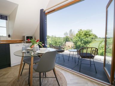 A dining area with a glass table set for two next to an open door leading to a balcony with two chairs and a table at Little Knaplock in Fiddington near Combwich Somerset