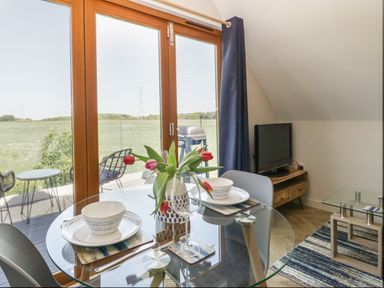 A dining area with a glass table set for two near large wooden framed windows with a view of green fields at Little Knaplock in Fiddington near Combwich Somerset