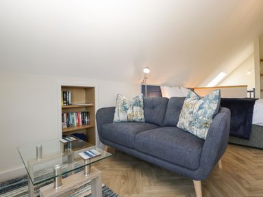 A sitting area with a blue sofa and patterned cushions glass coffee table and a small bookshelf at Little Knaplock in Fiddington near Combwich Somerset
