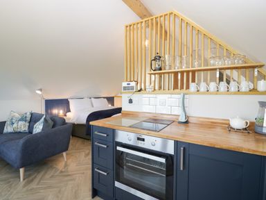 A kitchen with oven and blue cabinets next to a living area with blue sofa and a bed at Little Knaplock in Fiddington near Combwich Somerset