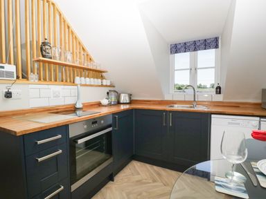 A kitchen with dark cabinets wooden countertops a glass stove oven a sink under a window and kitchenware on shelves at Little Knaplock in Fiddington near Combwich Somerset