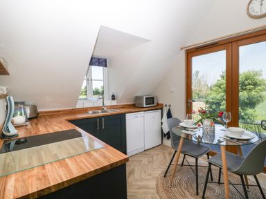 A kitchen with wooden countertops a sink microwave dishwasher dining table with chairs and glass doors overlooking greenery at Little Knaplock in Fiddington near Combwich Somerset