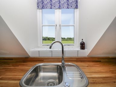 A kitchen sink with a chrome faucet below a window with a blue leaf-patterned curtain at Little Knaplock in Fiddington near Combwich Somerset