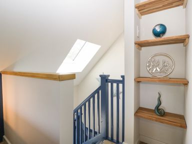 A staircase with blue railings next to wooden shelves with decorative items at Little Knaplock in Fiddington near Combwich Somerset