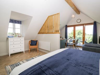 A bedroom with a bed a white dresser a wicker chair and a dining table near large glass doors at Little Knaplock in Fiddington near Combwich Somerset