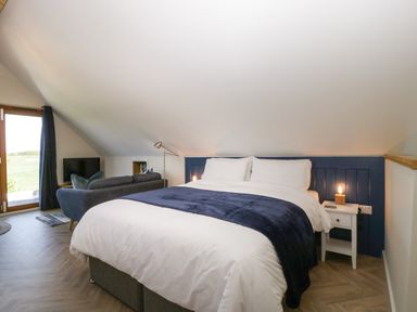 A bedroom with a double bed blue headboard and blanket a sofa and a television at Little Knaplock in Fiddington near Combwich Somerset