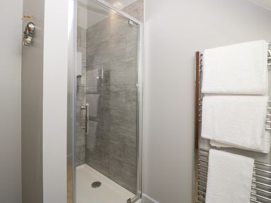 A bathroom shower with gray tiled walls and glass door next to a chrome towel rack with white towels at Little Knaplock in Fiddington near Combwich Somerset