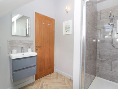 A bathroom with a gray sink cabinet mirror wooden door and a tiled shower at Little Knaplock in Fiddington near Combwich Somerset
