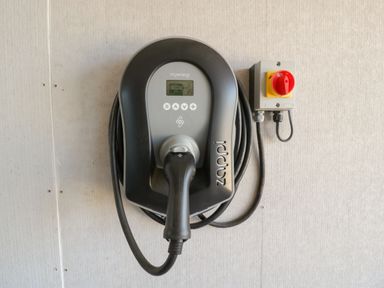 An electric vehicle charging station mounted on a wall with a coiled cable and a red switch at Little Knaplock in Fiddington near Combwich Somerset