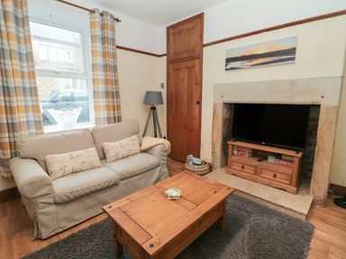 A living room with a beige sofa wooden coffee table and television on a stand in a stone fireplace at Coras House in Amble