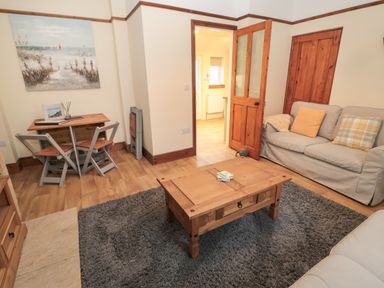 A living room with a wooden coffee table a gray rug a small dining table with chairs and a sofa with cushions at Coras House in Amble