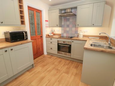 A kitchen with grey cabinets a wooden door a microwave a stainless steel oven and sink at Coras House in Amble