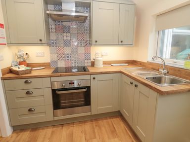 A kitchen with wooden countertops an oven a stovetop with a patterned tile backsplash a double sink and cabinets at Coras House in Amble
