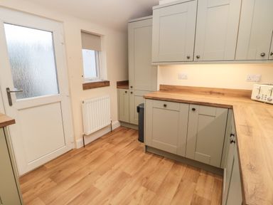 A kitchen with wooden countertops grey cabinets a white door and a window at Coras House in Amble