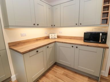A kitchen corner with wooden countertops gray cabinets a white toaster and a black microwave at Coras House in Amble
