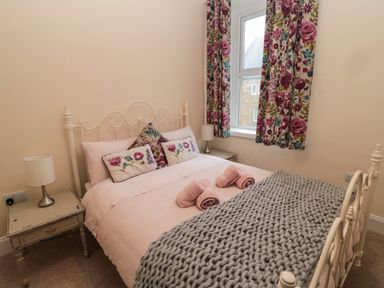 A bedroom with a bed with pink bedding and floral pillows next to a window with floral curtains at Coras House in Amble