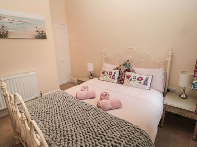 A bedroom with a white metal bed frame pink bedding rolled towels bedside tables lamps and a painting at Coras House in Amble