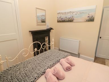 A bedroom with a metal bed frame a knitted blanket pink towels on the bed a radiator and a fireplace with a mirror and artwork above it at Coras House in Amble