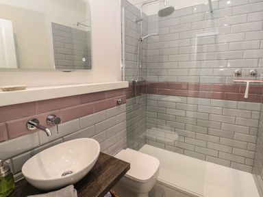A bathroom with a sink a toilet and a walk in shower with grey and pink tiled walls at Coras House in Amble