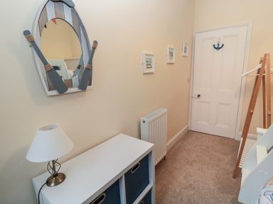 A hallway with a boat-shaped mirror a white cabinet with storage bins a lamp carpeted floor and a white door at Coras House in Amble