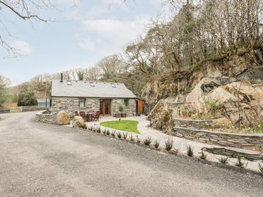 A stone cottage with outdoor table and chairs next to a rock face and garden at Tyn Llwyn Cornel Eco Barn in Garreg