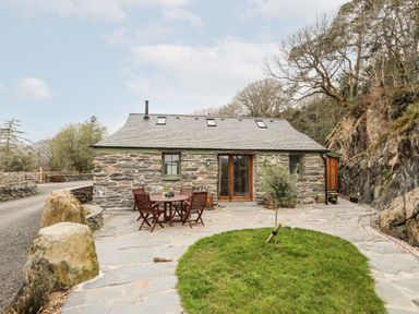 Stone cottage with a patio table and chairs and a small tree on a stone patio at Tyn Llwyn Cornel Eco Barn in Garreg