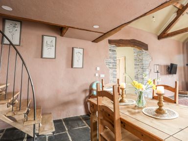 A dining area with a wooden table and chairs a stone floor spiral staircase and framed botanical prints on the wall at Tyn Llwyn Cornel Eco Barn in Garreg