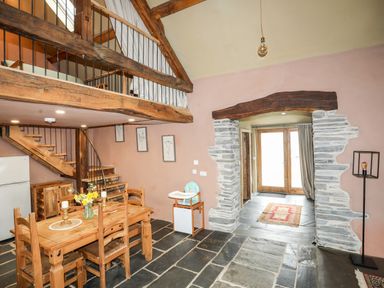 A dining area with wooden table and chairs stone flooring and a mezzanine with wooden railing at Tyn Llwyn Cornel Eco Barn in Garreg